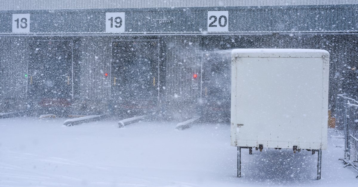 A loading dock at a warehouse. Bays 18, 19, and 20 are open. It is snowing very heavily outside.