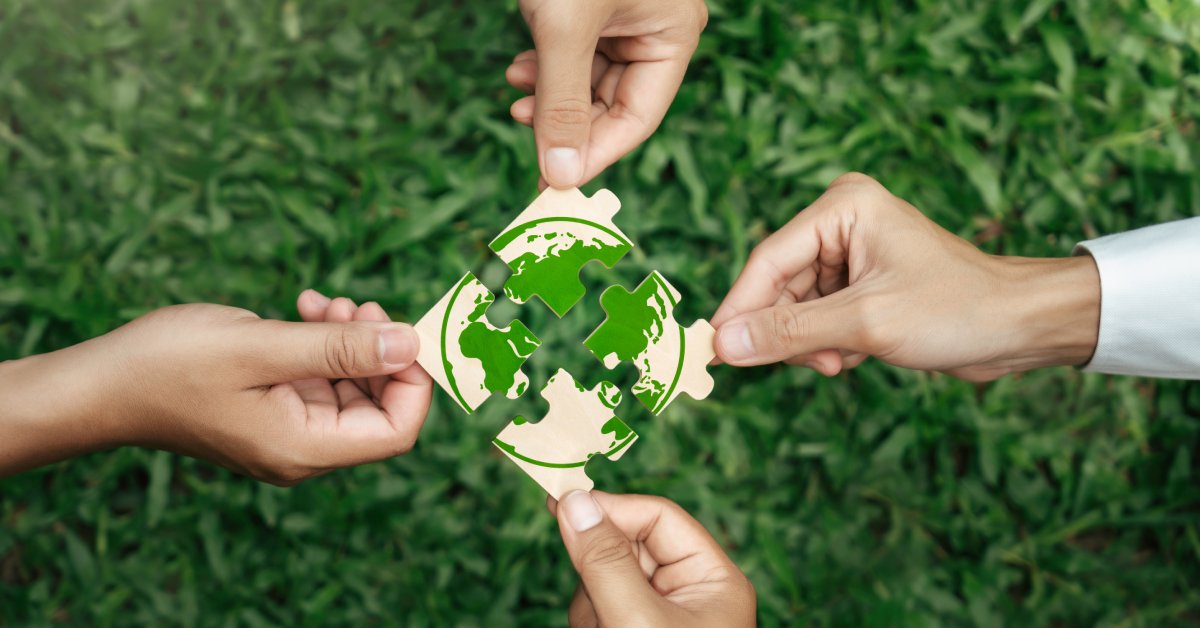 Four people each hold a puzzle piece in their hands. They put the pieces together to show a picture of a green earth.